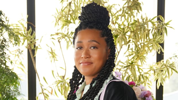 Naomi Osaka wears her hair in a bun on top of her head and smiles at the camera.